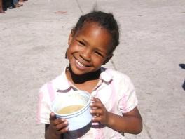 Smiling orphan child with AIDS in South Africa pictured with a bowl of sorghum food replacement supplement.