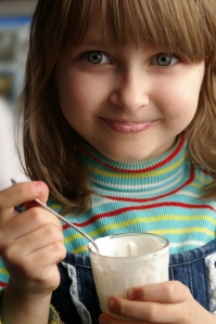 Beautiful Little USA Girl Eating High Sugar Impact Yogurt Snack.  Yogurt is a high sugar impact food and sadly low fat yogurt contains even more carbs making low fat yogurt an even higher sugar impact snack.  If fruit or sugar is added to the yogurt, the sugar impact increases even more.