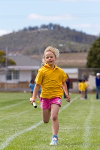 USA elementary age athlete carrying a baton and running in a relay race.