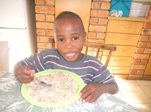 Elemenatary age orphan boy eating a plate full of sorghum based meal replacement.