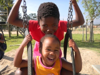 Two beautiful HIV victims orphans laughing and swinging on swing set in ghetto orphanage playground.